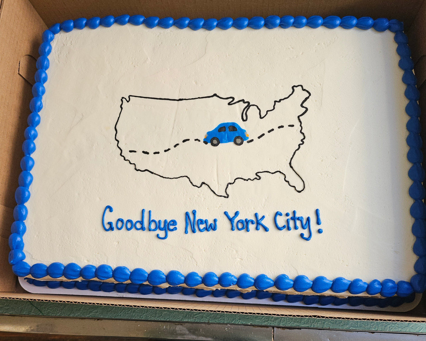 Sheet cake with a map of the United States and 'Goodbye New York City!' text, framed with blue icing.