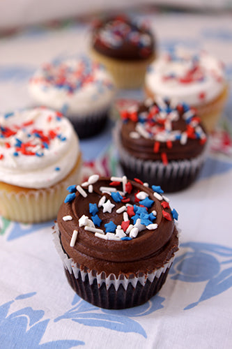 Cupcakes with chocolate frosting and red, white, and blue sprinkles on a floral tablecloth.