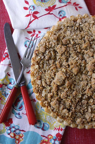 An apple crumb pie with an oatmeal crumb topping on a colorful cloth next to a knife and fork.