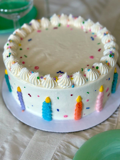 White birthday cake with colorful candles and sprinkles on a table.