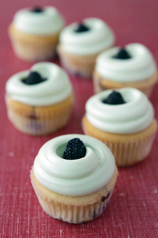 A group of cupcakes with white frosting and a blackberry on top, set against a red textured background.