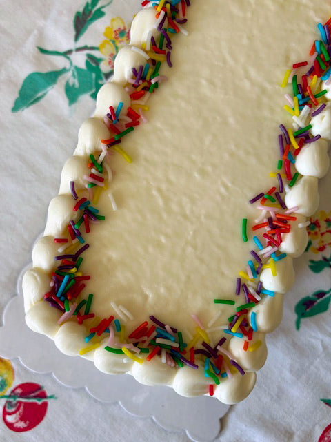 Decorative cake with white icing and colorful sprinkles on a floral tablecloth.