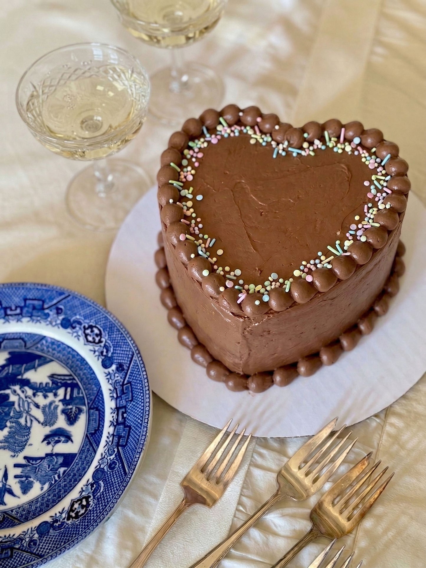 Heart-shaped chocolate cake with sprinkles on a table with plates and glasses.