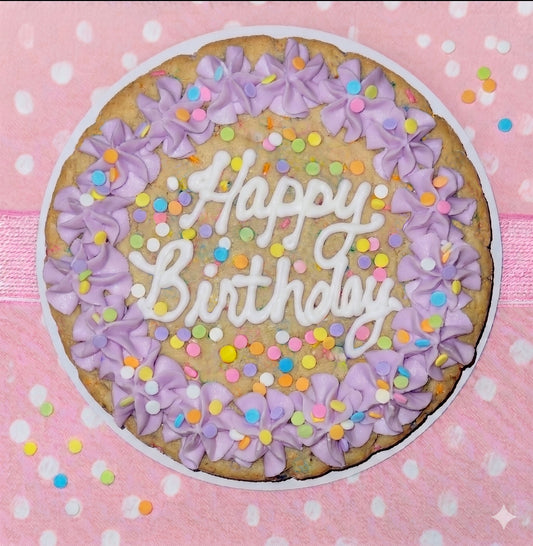 Cookie cake with 'Happy Birthday' text and purple frosting on a pink polka dot background