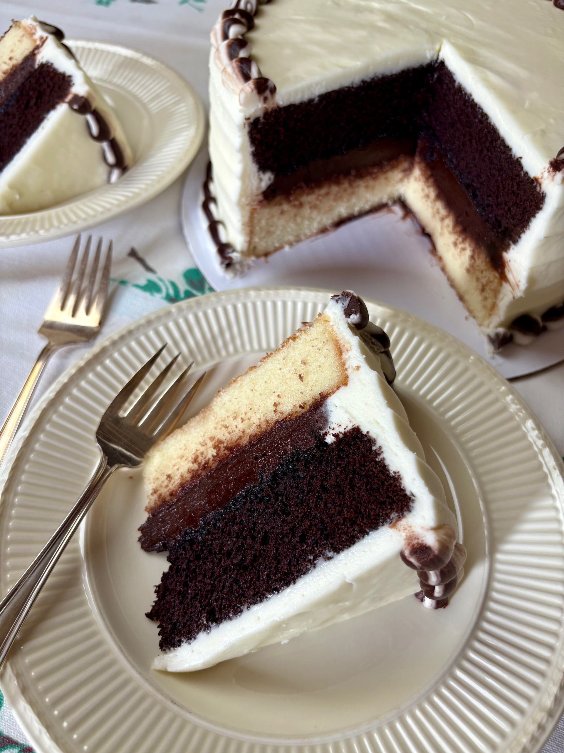 Chocolate cake with white frosting on a white plate with a fork, on a tablecloth.