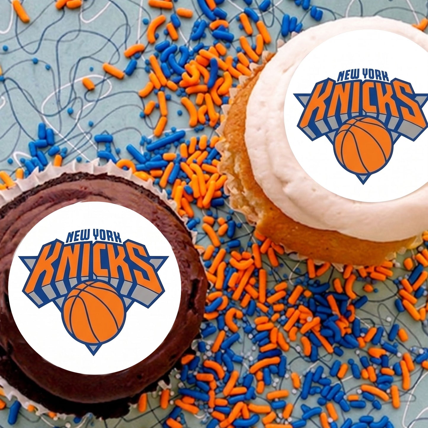 Two cupcakes with New York Knicks logo and colorful sprinkles on a textured surface