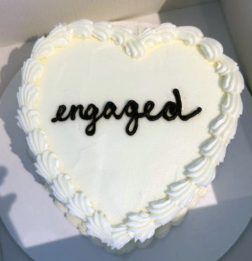 Heart-shaped cake with 'engaged' decoration on a white background