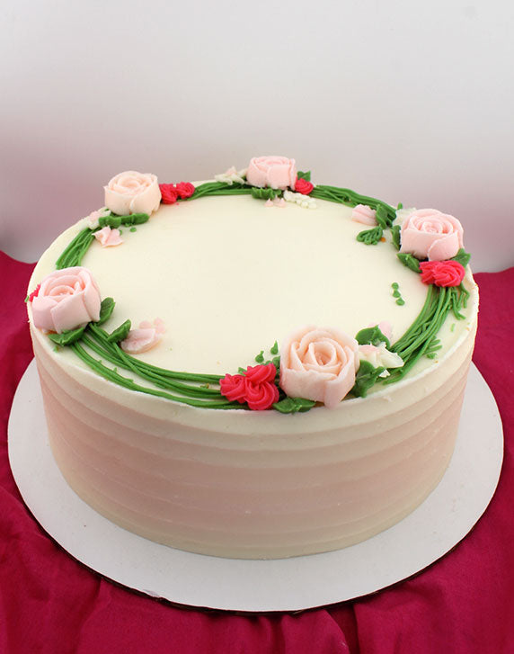 A round cake decorated with a garland of buttercream flowers in pink, red, and white colors, set against a red and white checkered background.