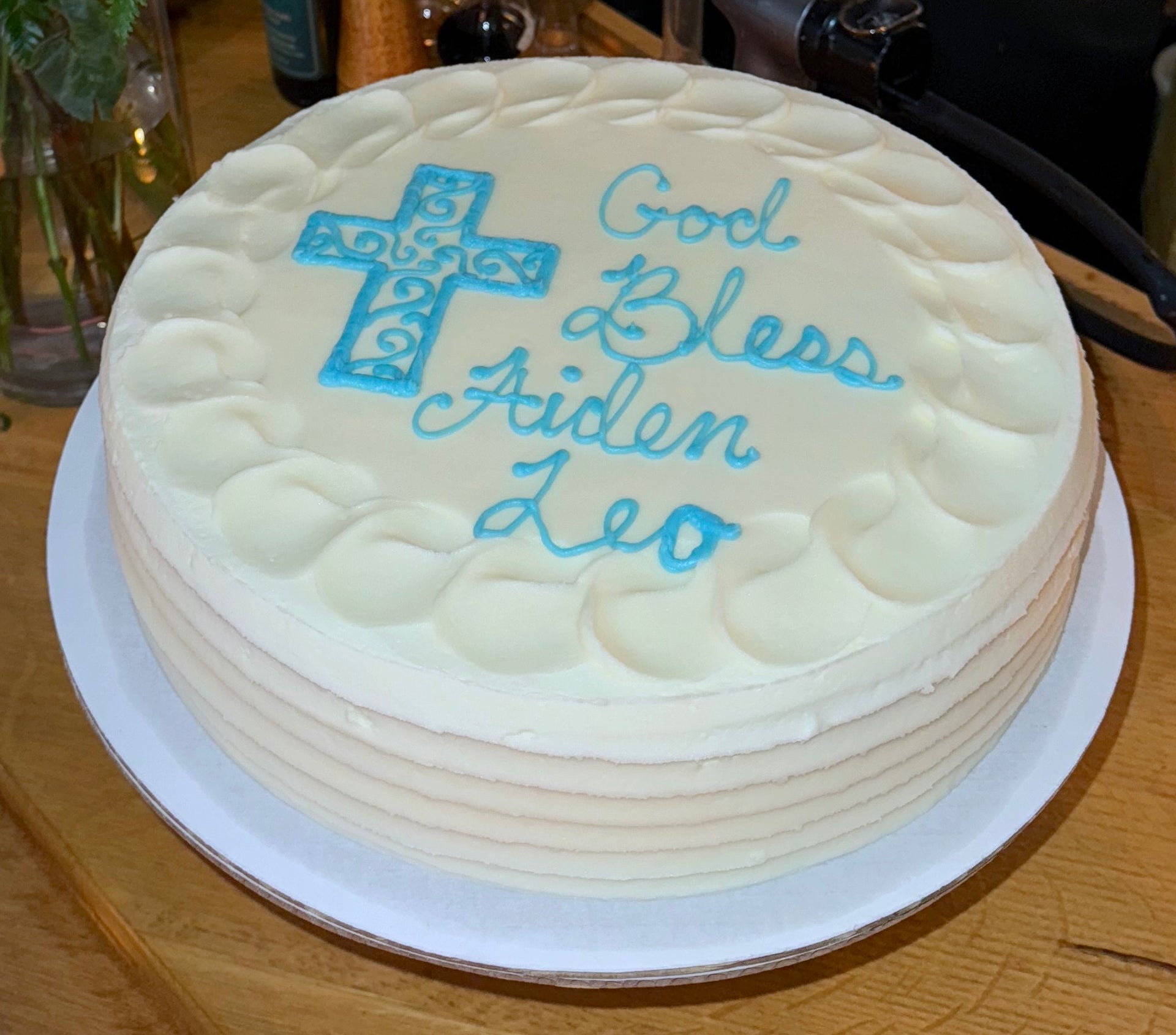 White cake with blue text and cross on a wooden table