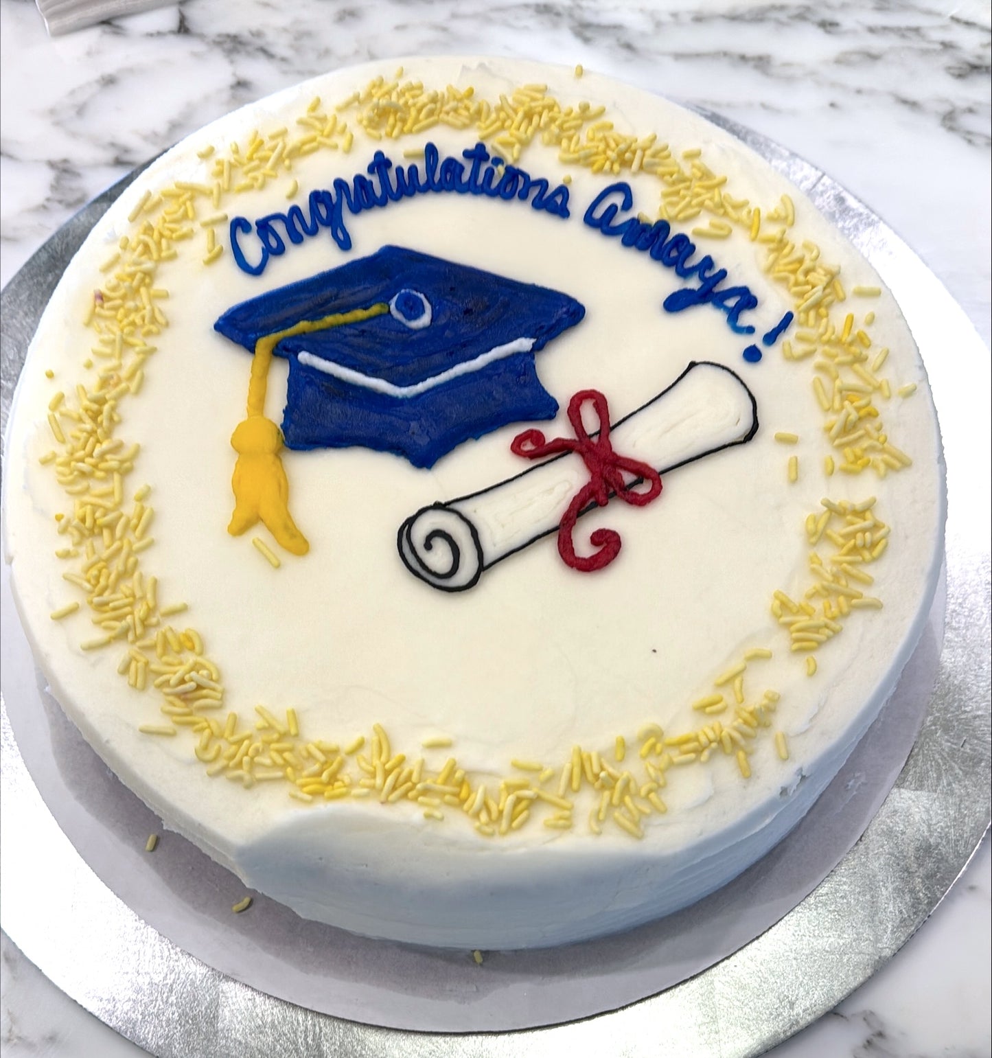 Graduation-themed cake with blue cap and red diploma on a white background