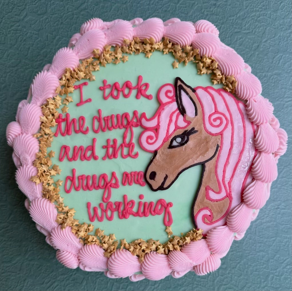 Decorative cake with pink icing, horse design, and text on a teal background