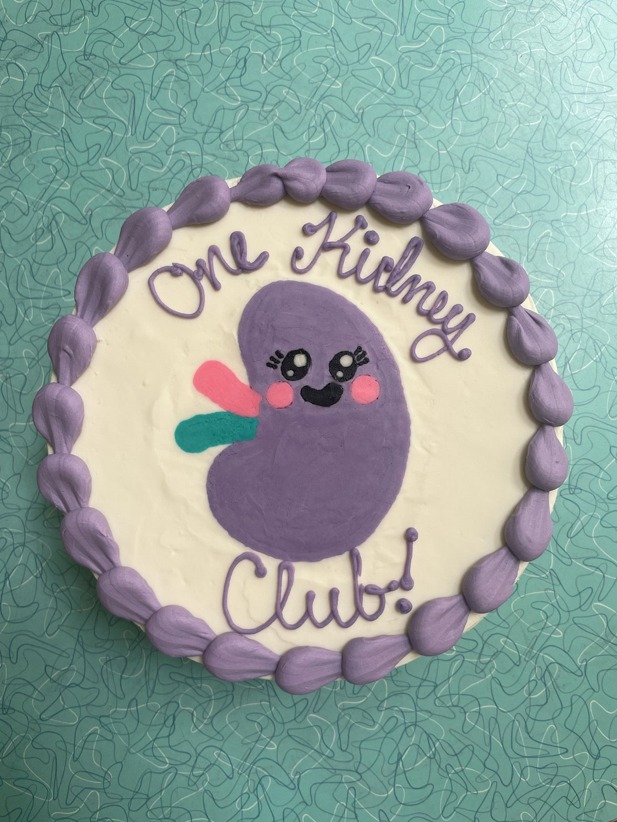 Cake with a purple character and 'One Kidney Club!' text on a textured green background
