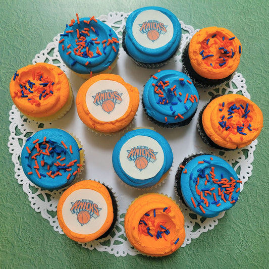 Cupcakes with orange and blue icing on a decorative doily against a green background