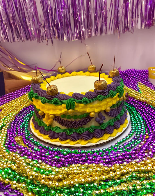 A decorative cake with yellow, green, and purple layers and yellow frosting piped in a floral pattern, topped with cherries and gold decorations.