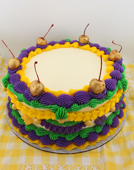 A multi-layered Lambeth cake with yellow, green, and purple frosting, decorated with cherries on top and edible fleur de lis sugar decorations.