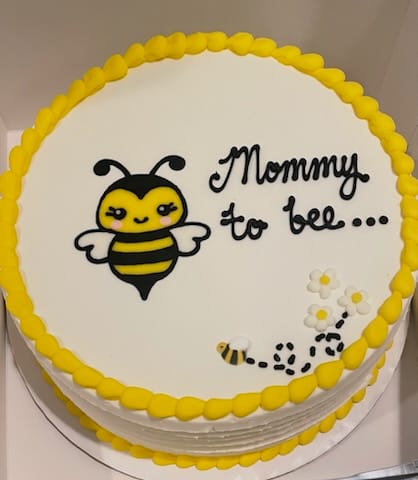 Round cake with a bee design and 'Mommy to be' text on a white background