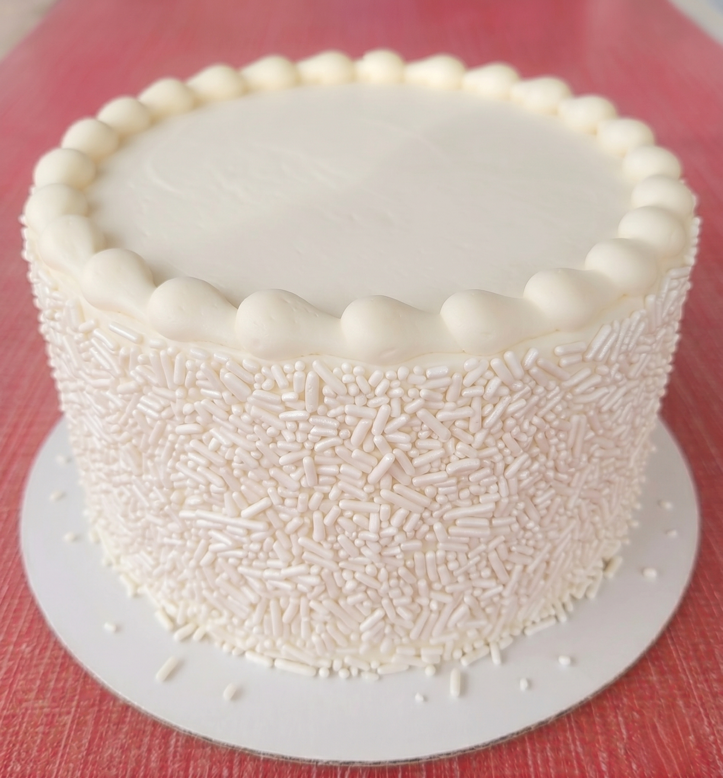 White cake with decorative sprinkles on a red surface
