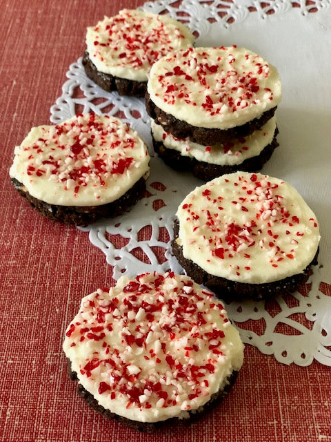 Four round peppermint white chocolate buttercream cookies on a lace doily with a red and green Christmas-themed pattern in the background.