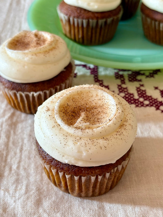 Pumpkin cupcakes with cream cheese frosting and cinnamon sugar dust on a textured surface.