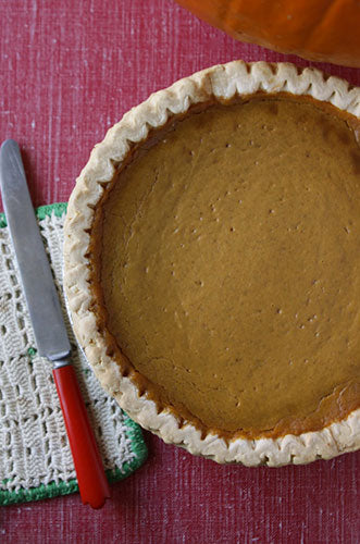 A baked pumpkin pie with a buttery crust on a red and green cloth, alongside a knife and a red spatula.
