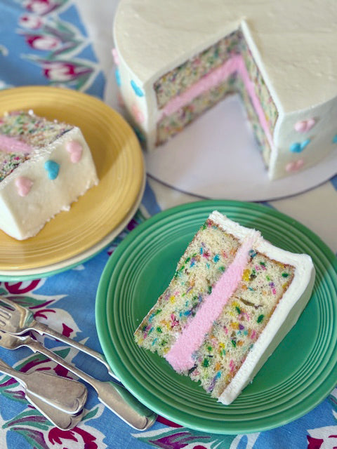 Colorful layered cake with a slice on a green plate, placed on a floral tablecloth.