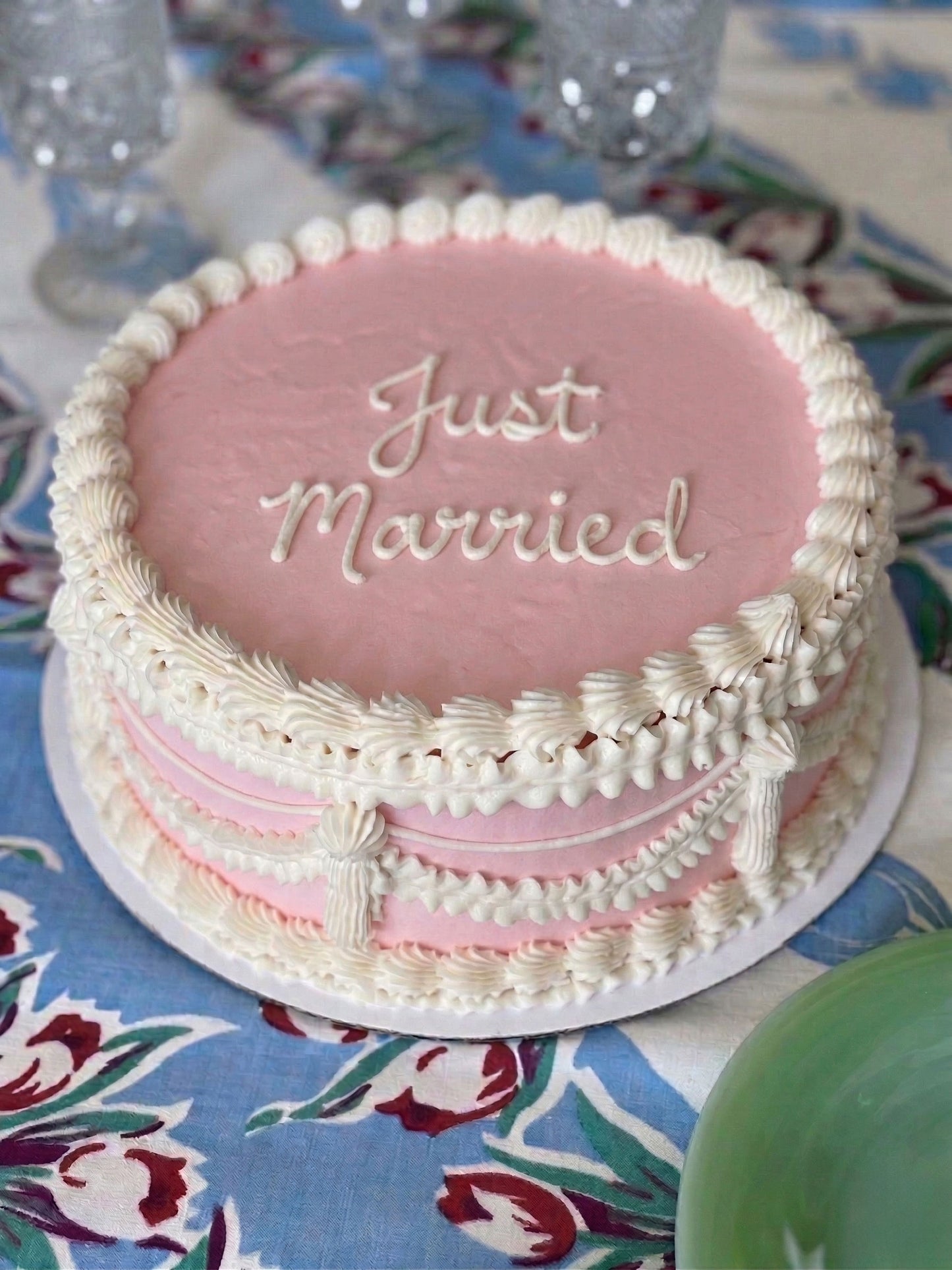 Pink wedding cake with 'Just Married' text on a floral tablecloth.