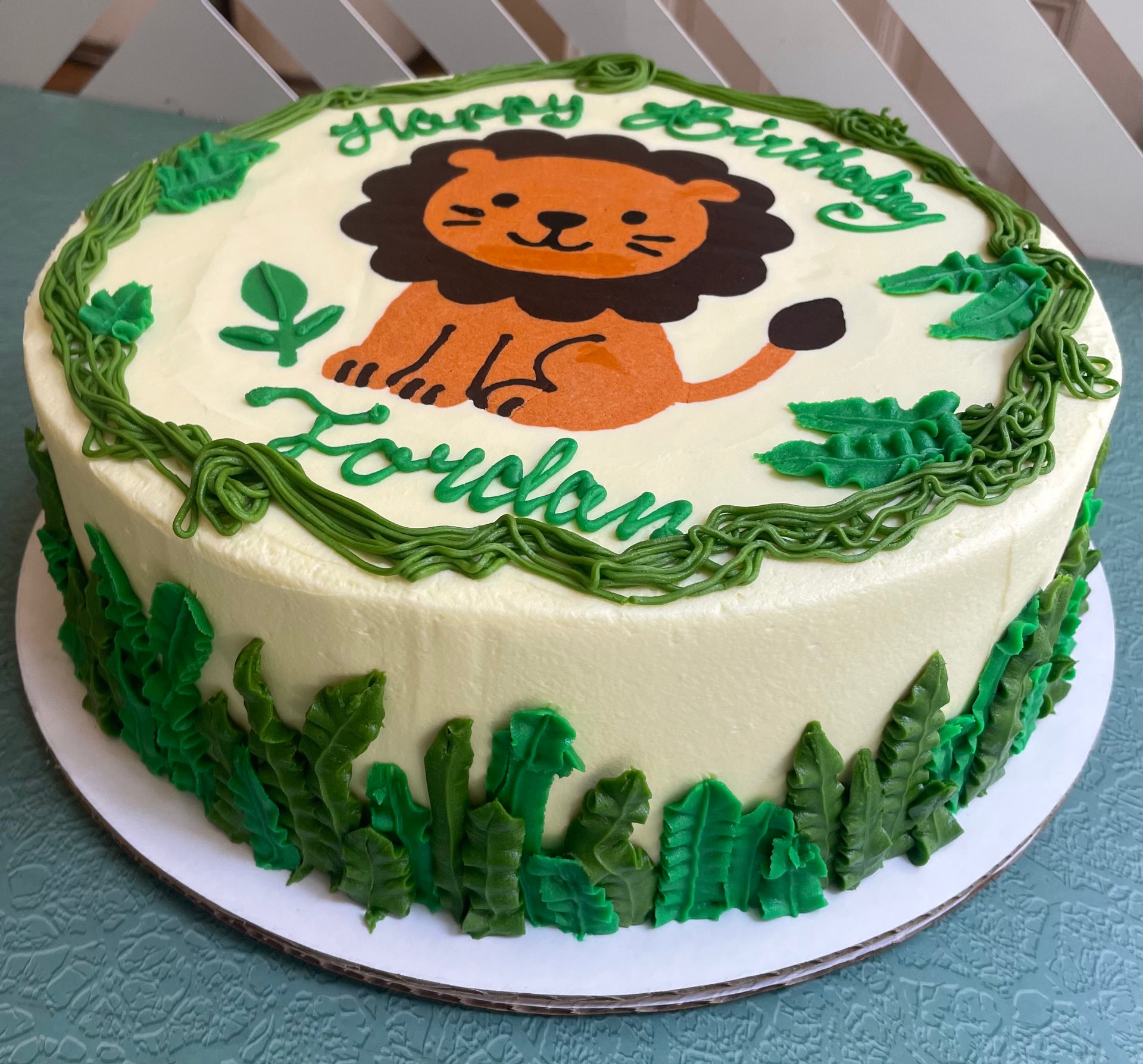Birthday cake with a lion design and green decorations on a white plate.