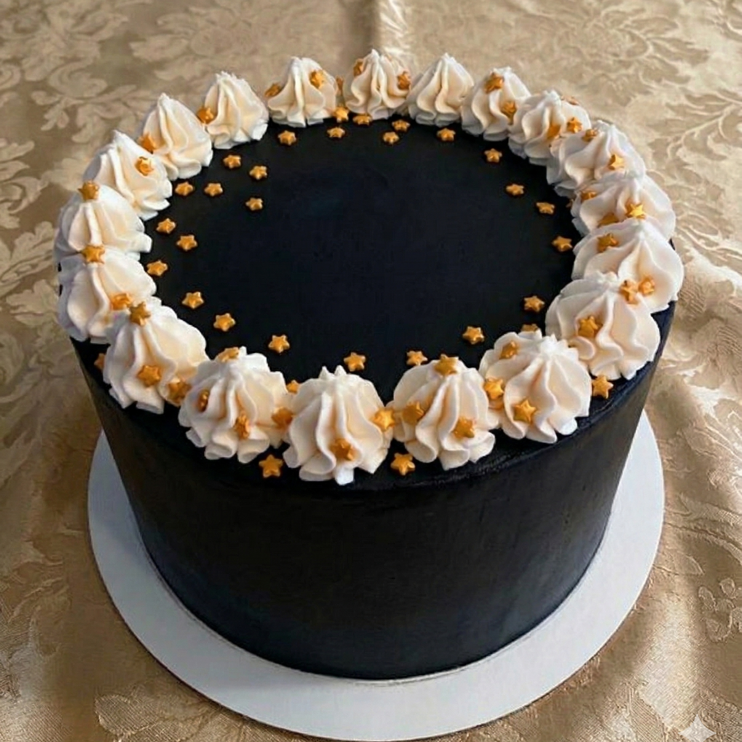Black cake with white frosting and gold decorations on a gold patterned tablecloth