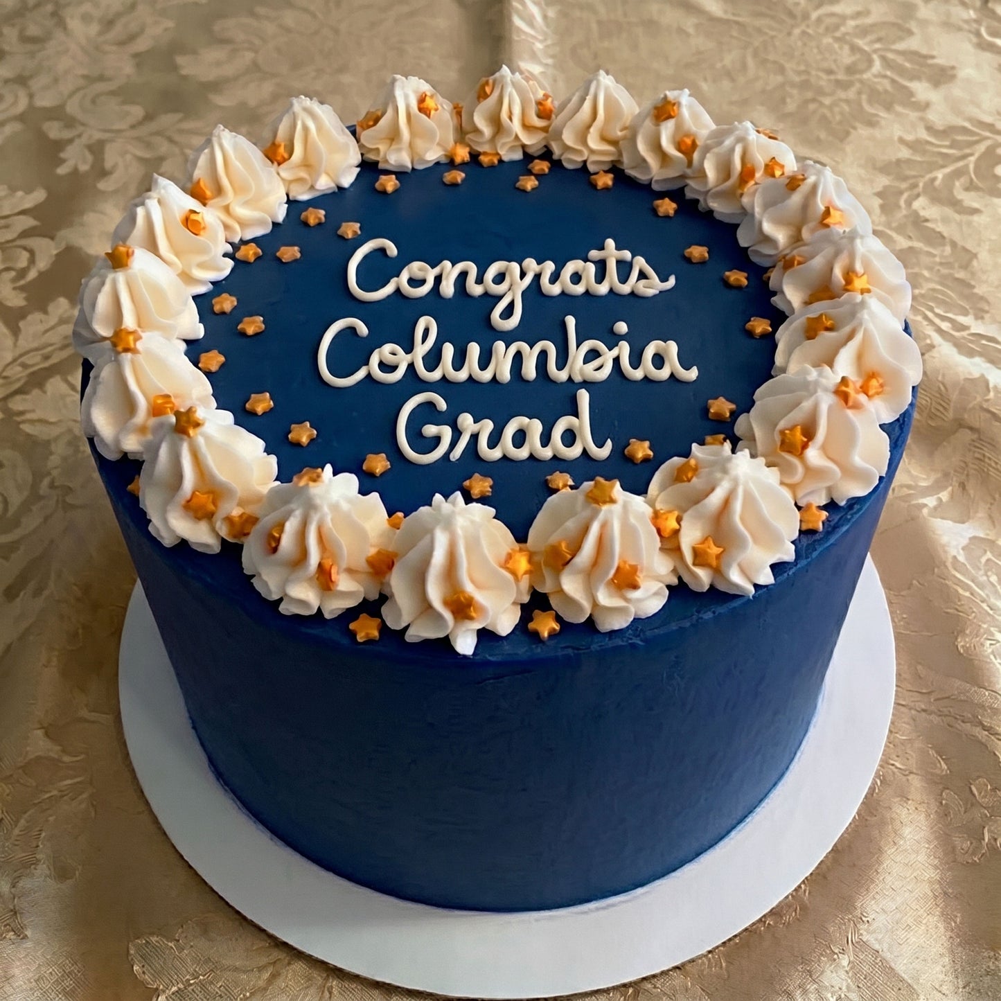Navy Blue cake with decorative white frosting and gold stars on a gold patterned tablecloth