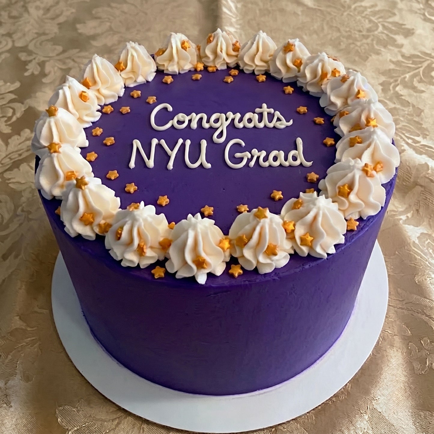 Bold Purple cake with decorative white frosting and gold stars on a gold patterned tablecloth
