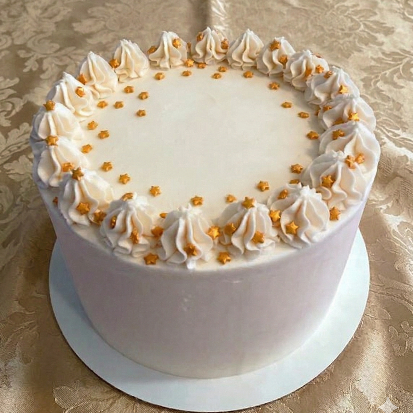 White cake with decorative white frosting and gold stars on a gold patterned tablecloth