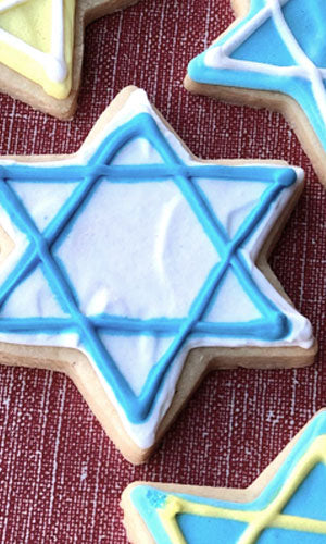 A sugar cookie cut into a Star of David shape, with a blue and white icing design on a red and blue background.