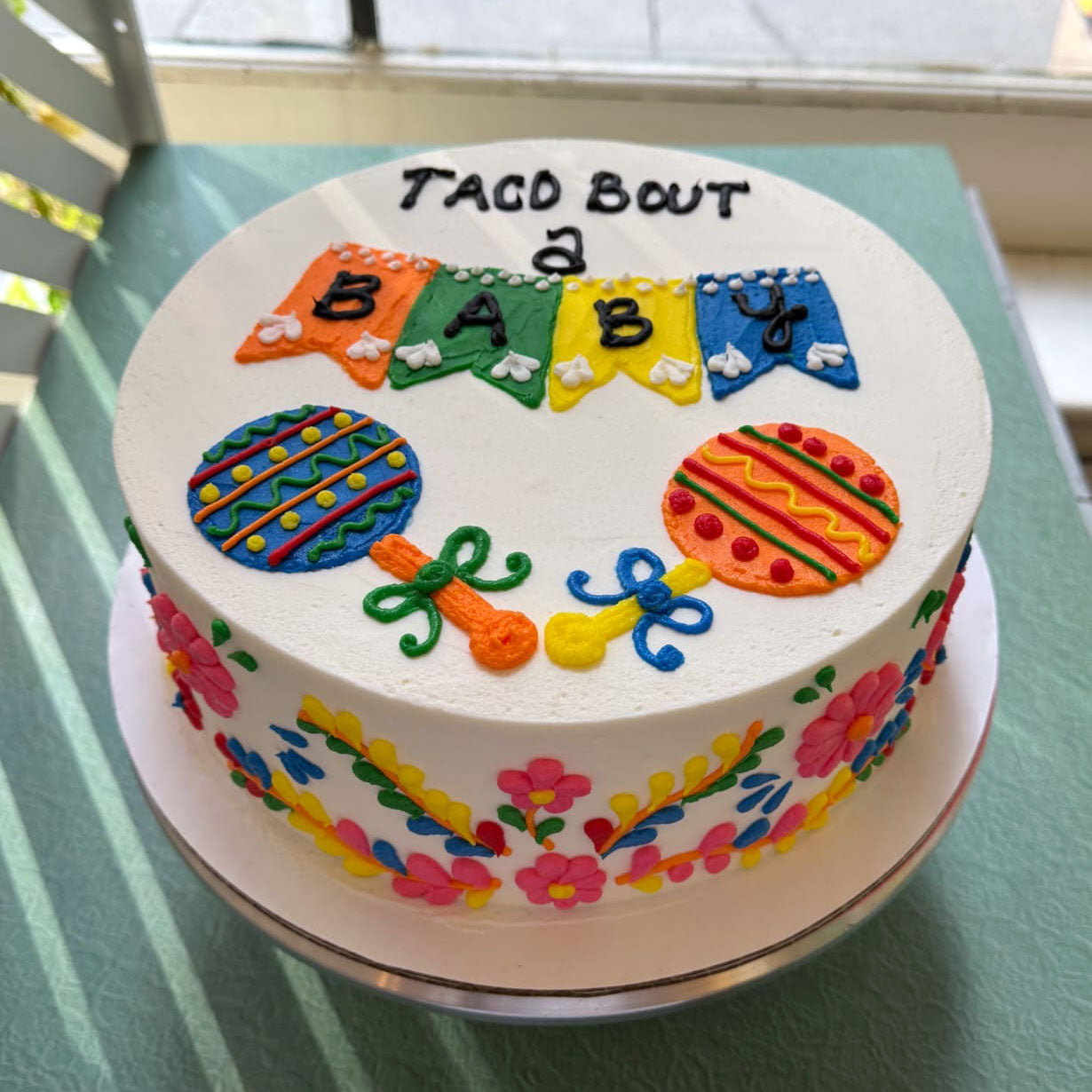 Colorful baby shower cake with 'Taco Bout a Baby' text on a green table.