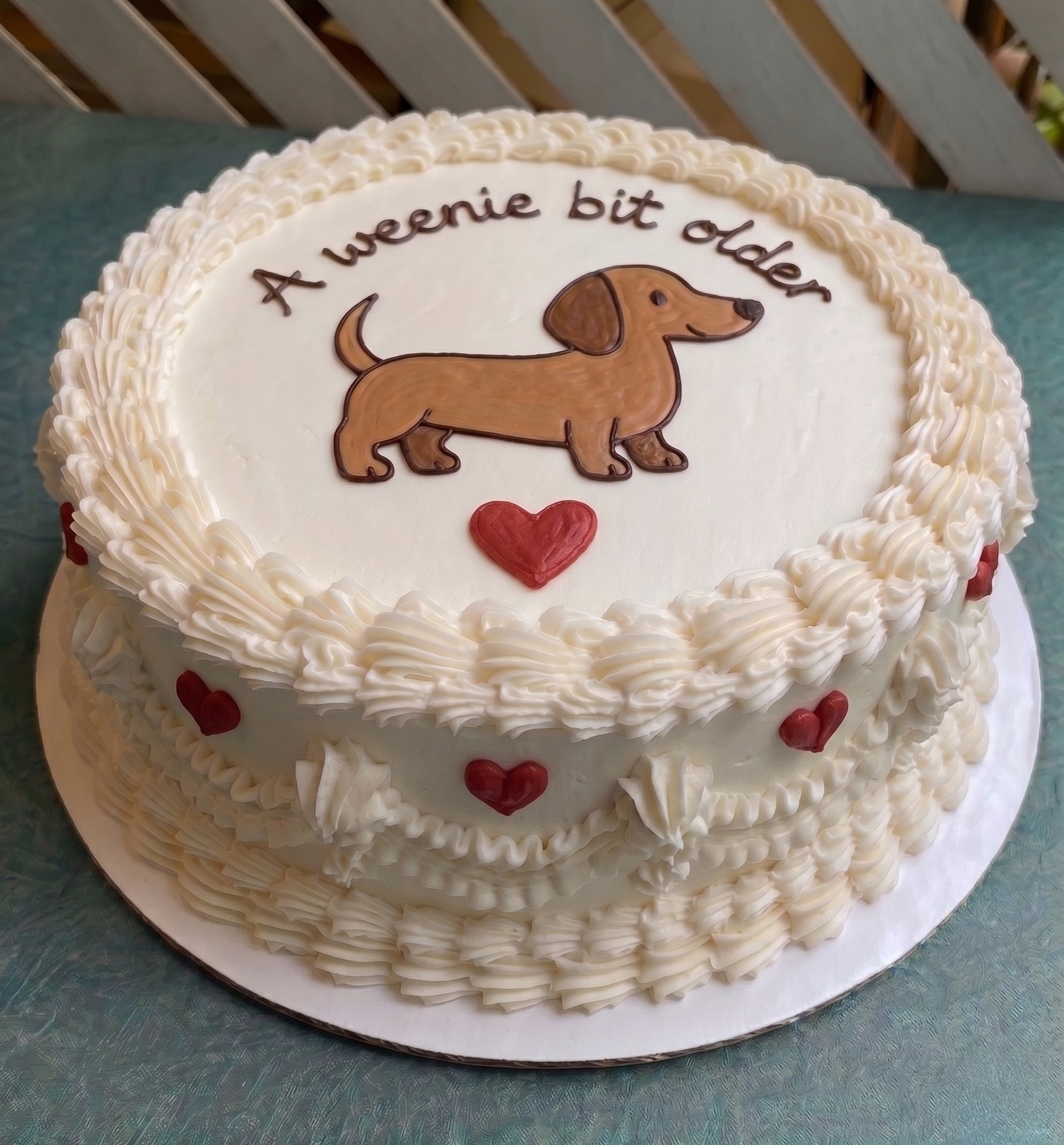 Birthday cake with dachshund illustration and text 'A weenie bit older' on a white background.