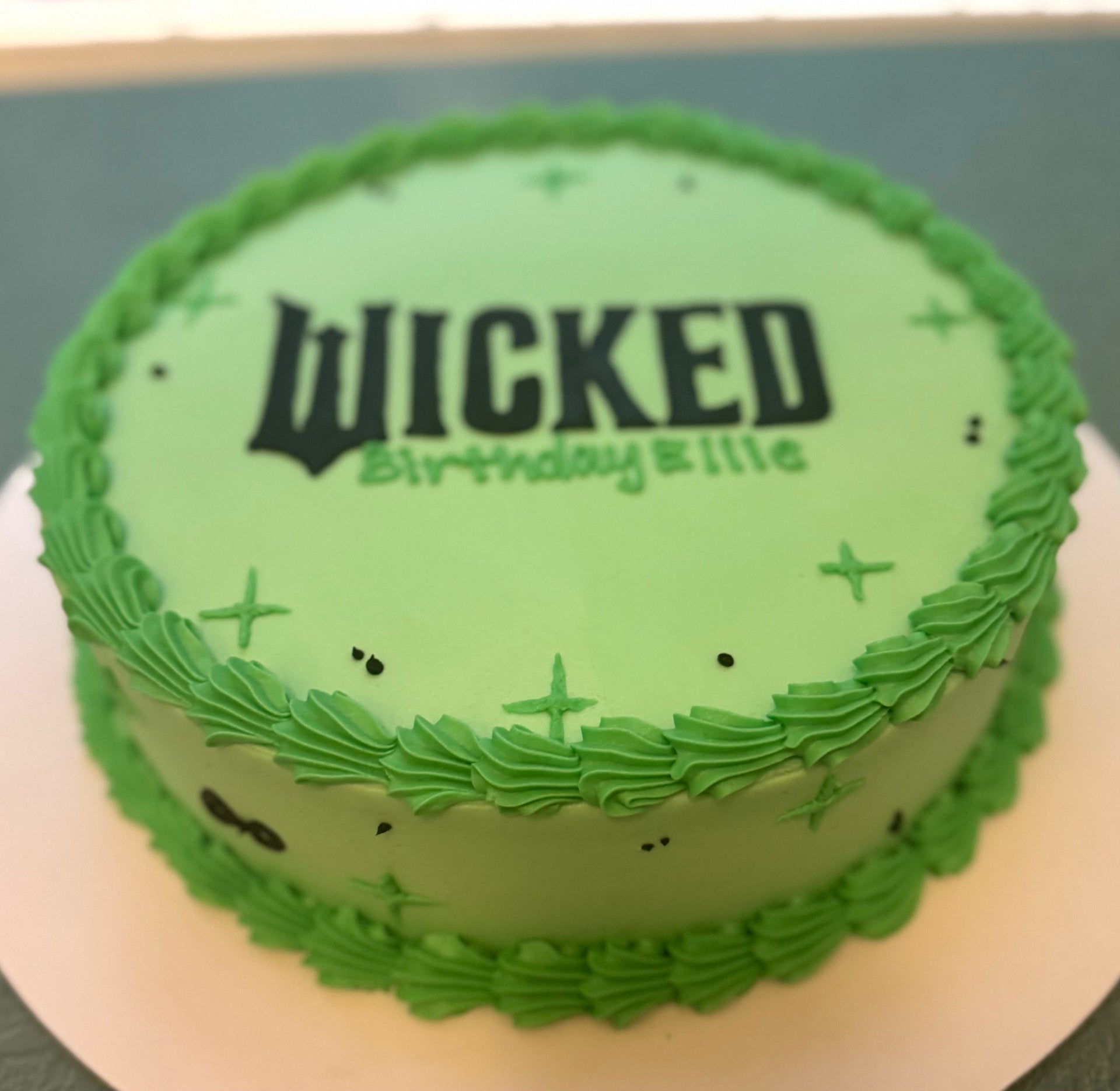 Green birthday cake with 'Wicked' text on a white plate
