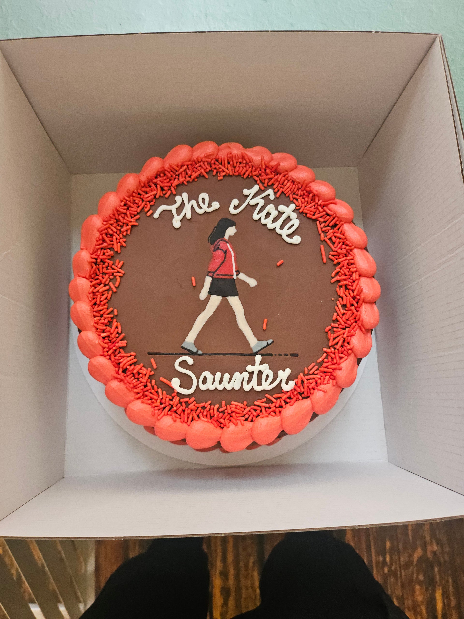 Cake with a design of a person skateboarding and text 'The Skate Saunter' on top of a box.