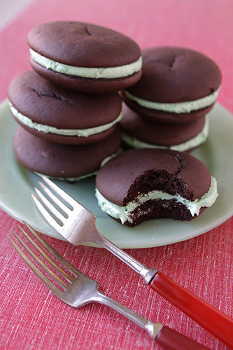 Stacked chocolate mint whoopie cakes on a plate with a fork, with one whoopie cake cut in half to show the filling.