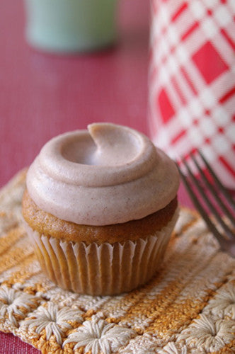 A close-up of a pumpkin cupcake with light pink frosting on a crocheted placemat.